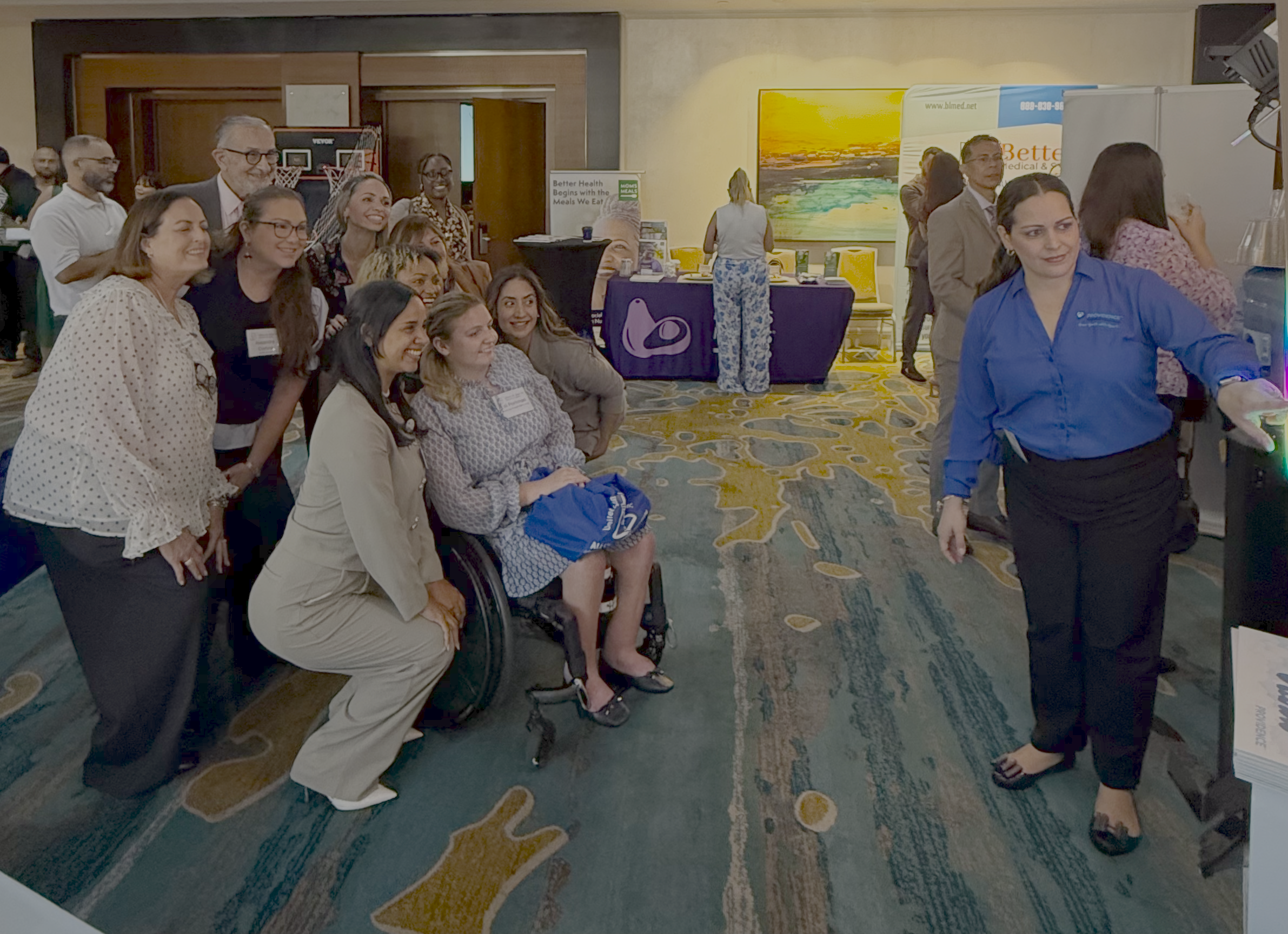 Group of diverse attendees posing for a photo at an expo, with booths and banners in the background.